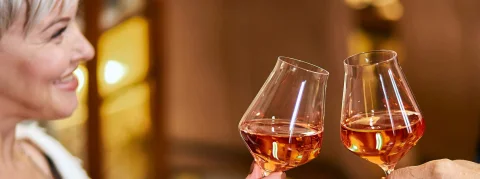 Zwei Glas Rosé Wein stossen an, links lächelt eine Frau